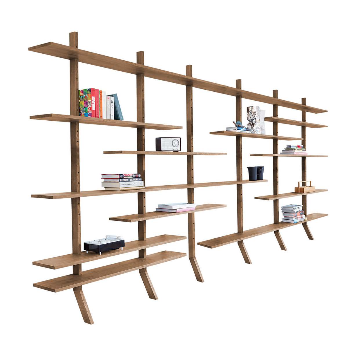 Janua KS 01 Regalsystem aus Eiche mit versetzten Regalbrettern und schräg gestellten Füßen, mit Büchern dekoriert – schräg von vorn